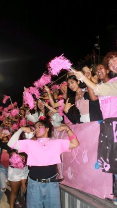 a group of people standing next to each other holding up pink signs and cheerleaders