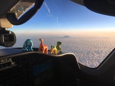 three toy dinosaurs are sitting in the cockpit of an airplane, looking out over the clouds