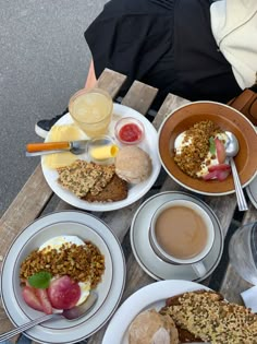 a table topped with plates of food next to cups of coffee and juices on top of wooden boards