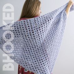 a woman holding up a crocheted shawl in front of a white wall