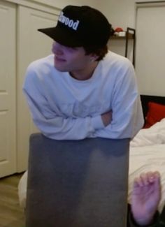 a young man sitting on top of a bed wearing a hat