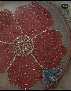 a large red flower is on a glass plate with gold rivets and sequins