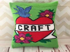 a green pillow with a red heart and flowers on it that says craft next to a white chevron wall