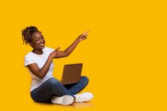 a woman sitting on the floor with her laptop pointing at something in front of her