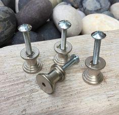 three metal screws are sitting on a piece of wood next to some rocks and stones