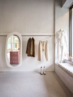 clothes hanging on the wall next to a mirror and shoe rack in a room with large windows