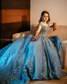 a woman in a blue dress sitting on a couch with her hand on the arm