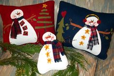 three snowmen are sitting on pillows with christmas tree branches in the foreground and one is wearing a scarf