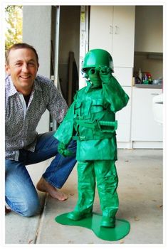 a man kneeling down next to a green toy soldier