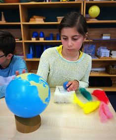 two children are sitting at a table painting the earth