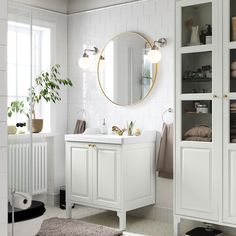 a bathroom with white cabinets and a round mirror