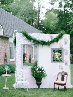 a chair sitting in the grass next to a small white building with flowers on it