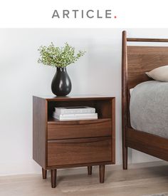 a nightstand with a vase on it next to a bed