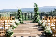 an outdoor ceremony set up with wooden chairs and white flowers on the aisle, overlooking mountains