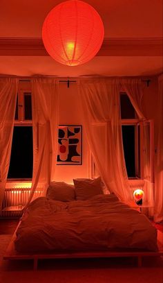 a bed sitting under a red light in a bedroom next to two windows with curtains