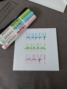 some markers and pens are sitting on a table next to a happy birth day card