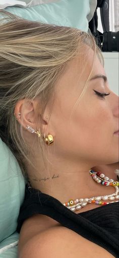 a woman laying in bed with her eyes closed wearing some earrings and beads on her neck