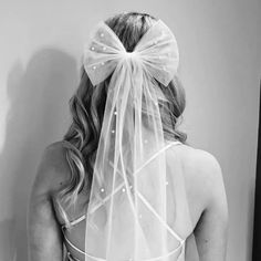 the back of a bride's dress with a veil on her head and a bow in her hair