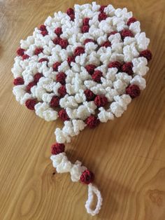 a crocheted umbrella with red and white flowers on the top is laying on a wooden table