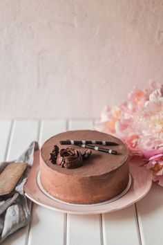 a chocolate cake sitting on top of a white plate next to pink and white flowers