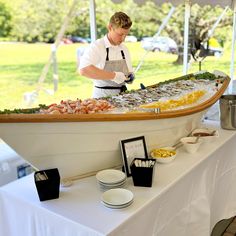 a man standing in front of a boat filled with food on top of a table