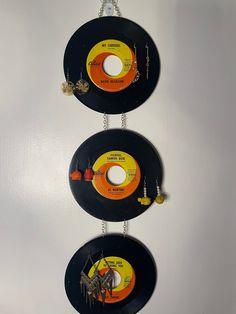 three black records hanging from chains on a white wall with orange and yellow discs attached to them