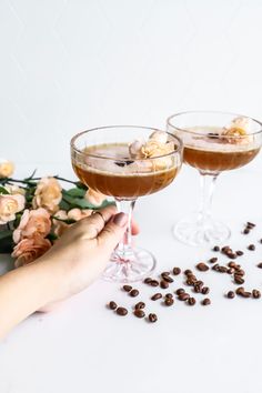 two wine glasses filled with coffee and topped with flowers on a white table next to pink roses