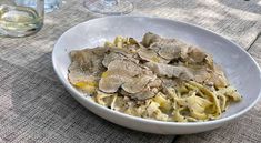 a white bowl filled with pasta and mushrooms on top of a table next to wine glasses