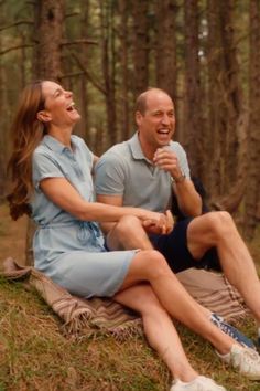 a man and woman laughing while sitting on a blanket in the middle of a forest