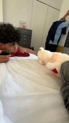 a young boy laying on top of a bed next to a teddy bear