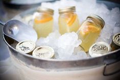 three jars filled with lemonade sitting on top of ice in a metal bowl next to spoons