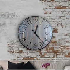 a large clock mounted to the side of a white brick wall next to a couch