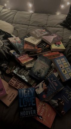 a pile of books sitting on top of a bed next to a pillow covered in blankets