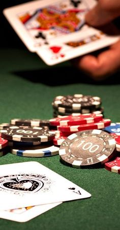 several poker chips and playing cards on a green table with one hand holding the other