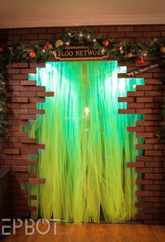 a brick wall with green sheer curtains and lights on the top is decorated with greenery