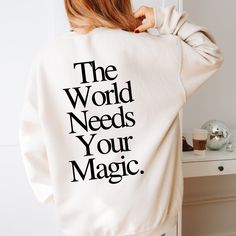 a woman with her back to the camera wearing a sweatshirt that says the world needs your magic