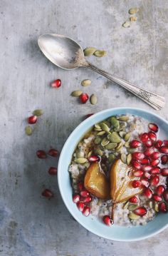 a bowl filled with oatmeal and pomegranate next to a spoon