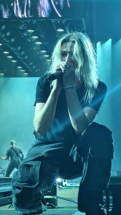 a man sitting on top of a stage with his hands to his face while holding a microphone