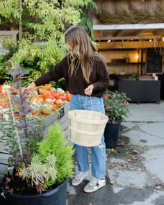 a woman holding a bucket full of fresh produce in front of an outdoor garden store