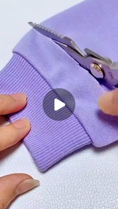 someone cutting fabric with scissors on top of the purple material that's being sewn