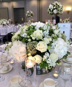 the centerpiece is surrounded by white flowers and greenery, along with tea cups and saucers