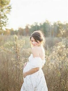 a pregnant woman standing in tall grass with her hands on her belly