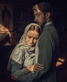 a man and woman embracing each other in a dark room with sunlight streaming through the window