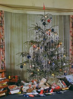 a christmas tree is surrounded by presents and other holiday items in front of a curtained window