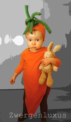 a baby dressed in an orange outfit holding a stuffed animal and wearing a carrot hat