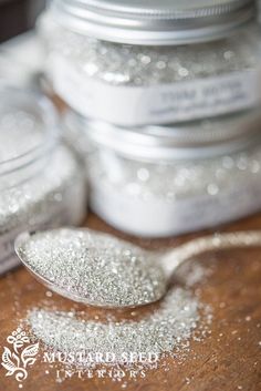 a spoon full of silver glitter sitting on top of a wooden table next to some jars