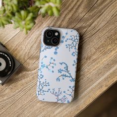 an iphone case sitting on top of a wooden table next to a camera and plant