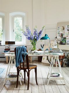 a chair and table in a room with white walls, wood flooring and large windows