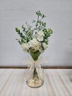 a clear vase with white flowers and greenery