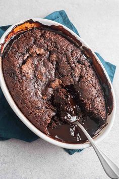 a chocolate cake in a white dish on a blue napkin with a spoon next to it